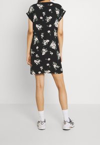 Robe noire à fleurs avec des manches courtes, une coupe décontractée et une longueur au genou. Le motif comprend des accents floraux roses et verts.