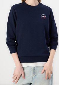 Navy blue sweatshirt made of cotton blend, featuring long sleeves, round neckline, ribbed cuffs, and a small logo design on the chest.