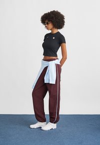 Crni skraćeni top, bordo hlače s svijetloplavim bočnim trakama i bijele tenisice. Svijetloplava dukserica vezana oko struka; teksturirana kosa.