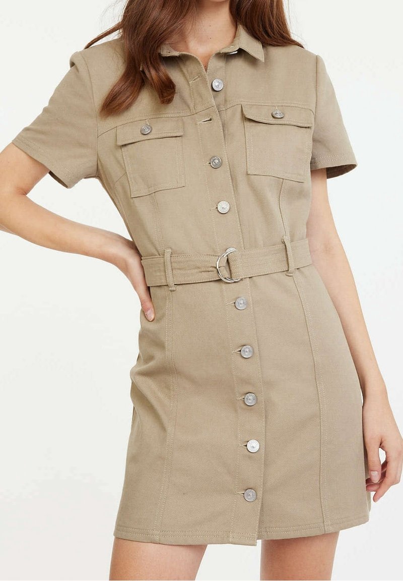 Khaki lyhythihainen mekko, jossa on kaksi rintataskua, vyötäröllä vyö ja nappilista, jossa on hopeiset yksityiskohdat ja muotoiltu siluetti.