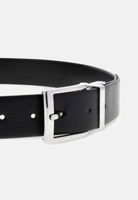 Ceinture en cuir noir avec une finition texturée, dotée d'une boucle en métal argenté et de trous pour l'ajustement, présentée en angle.