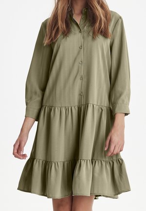 Abito verde oliva con bottoni, con strisce verticali, maniche lunghe e orlo fluttuante arricciato. Realizzato in un tessuto morbido con una vestibilità comoda.