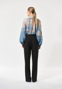 Lichtblauwe sheer blouse met bloemenpatroon, hoge nek en volumineuze mouwen, gecombineerd met zwarte op maat gemaakte broeken. Achteraanzicht, gladde textuur.