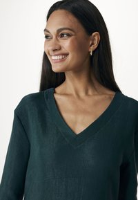 Zielony prążkowany top z dekoltem w kształcie litery V i długimi rękawami. Tkanina ma subtelny połysk i teksturowany wygląd.