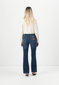 Jeans s bootcut krojem u tamnoplavom denimu, s visokim strukom, stražnjim džepovima sa šavnim detaljima i suptilnom kožnom etiketom na struku.