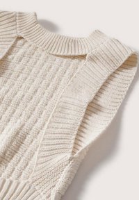 Jasnokremowy bezrękawnik z dzianiny, z prążkowanym dekoltem i teksturowanym ciałem, z diagonalnymi wzorami i szerokimi ramiączkami.
