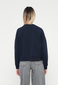 Felpa blu navy con spalle cadute, scollatura rotonda e design cropped. Il tessuto appare morbido, adatto per un abbigliamento casual.