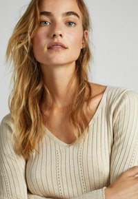 Maglione a coste beige chiaro con scollo a V, caratterizzato da una texture verticale, strisce sottili e una silhouette aderente. Tessuto morbido a maglia.