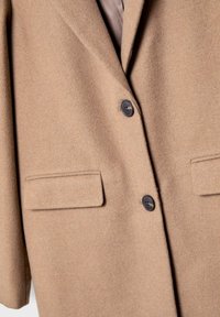 Manteau en laine marron avec deux boutons noirs et deux poches à rabat, vue de face, au centre.
