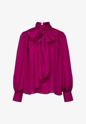 Blouse magenta avec un col haut et un grand nœud décoratif, présentant de longues manches bouffantes et des poignets à boutons. Fabriquée en tissu doux et lisse.
