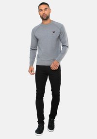 Grå crewneck sweatshirt med ribbede manchetter og kant, med et lille mørkt logo på brystet; parret med sorte skinny jeans og mørke sneakers.