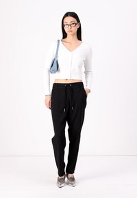 Top corto a maniche lunghe bianco a coste, pantaloni neri con coulisse, scarpe argento e borsa blu. Design semplice e vestibilità comoda.