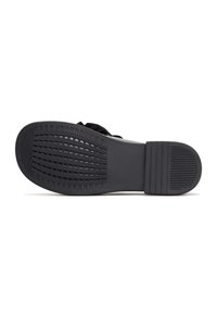 Semelle de chaussure noire avec motif de bande de roulement texturé pour l'adhérence, talon plat avec rainures horizontales, isolée sur fond blanc.