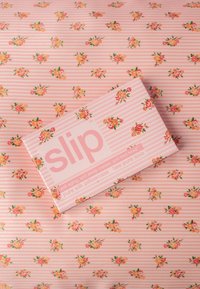 Verpackung eines Kissenbezugs aus rosa gestreiftem Seidenstoff mit kleinen Blumenmustern, platziert auf einem passenden floralen und gestreiften Stoffhintergrund.