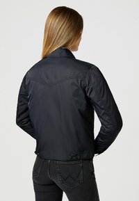 Schwarze, taillenlange Jacke mit strukturiertem Kragen und Schulternähten. Glattes, glänzendes Material mit Knopfdetails auf der Rückseite.