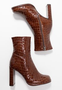 Bottes basses en cuir marron embossé crocodile avec une finition brillante, un talon bloc haut et une fermeture éclair latérale. Design angulaire et motif texturé.