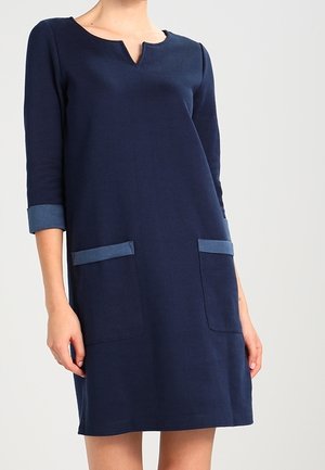 Mørkeblå knælængde kjole med trekvartærmer, V-udskæring og to forlommer med lysere blå kant.
