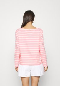Maglietta a maniche lunghe in cotone a righe rosa e bianche con scollo rotondo e vestibilità rilassata, abbinata a pantaloni corti bianchi.