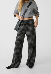 Mustavalkoruudulliset housut, jotka ovat väljät, joustovyötäröllä ja nyörillä varustetut. Yhdistetty harmaaseen lyhytmalliseen neulepuseroon ja mustaan laukkuun.