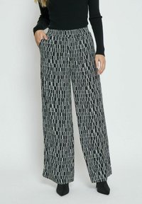 Wide-leg pants in a black and white geometric pattern, featuring an elastic waistband, side pockets, and a lightweight fabric.