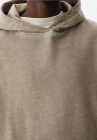 Sudadera beige hecha de un suave mezcla de algodón, con un bolsillo canguro y un ajuste relajado. Tejido texturizado con un ligero brillo.