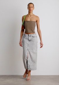 Ruda strapless viršūnė su sidabriniais mygtukais, derinama su šviesiai pilku džinsiniu sijonu su aukštu skeltuku. Modelis dėvi skaidrius šlepetes su dirželiu ir žalią diržinę rankinę.