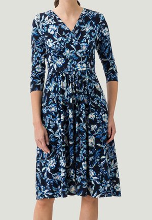 Femme portant une robe bleu marine longueur genou avec un imprimé floral blanc et bleu et manches trois-quarts.