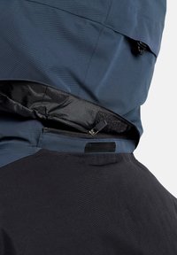 Wasserabweisende Jacke mit oberem Abschnitt in Marineblau, unterem Abschnitt in Schwarz, seitlichem Reißverschluss und Klettverschluss-Akzenten für eine verstellbare Passform.