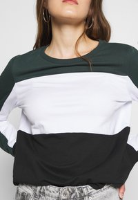 Långärmad topp med gröna, vita och svarta färgblock, med rund halsringning och mjukt bomullstyg. Strukturerad svart nedre del.