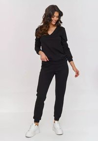 Czarny dres składający się z bluzy i spodni dresowych, z dekoltem w serek, ściągaczami na rękawach i miękką strukturą, zestawiony z białymi trampkami.