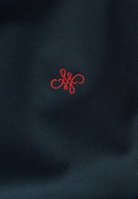 Tengerészeti szövet, piros hímzett monogramos mintával, bonyolult hurkokkal és formákkal. Simára csiszolt textúra, kompakt és sűrű szövés.