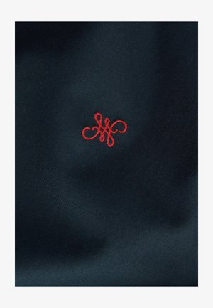 Tessuto blu navy con un design di monogramma ricamato in rosso, caratterizzato da intricate spirali e forme. Texture liscia, con un motivo compatto e fitto.