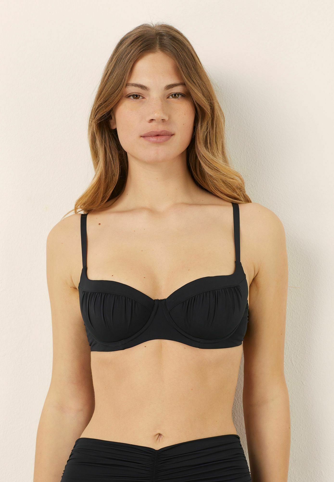 Czarny top bikini z fiszbinami, z marszczonym wzorem i regulowanymi cienkimi ramiączkami, wykonany z gładkiego elastycznego materiału.