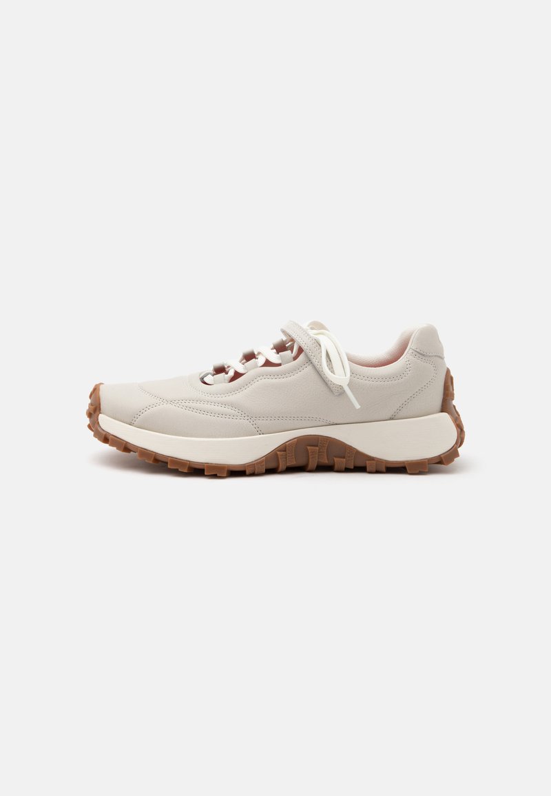 Baskets beige clair avec des lacets blancs, une bande auto-agrippante et une semelle épaisse en caoutchouc marron avec des rainures profondes pour une meilleure adhérence.