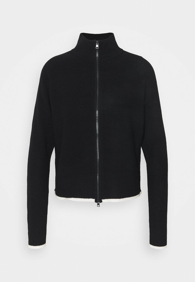 Veste noire en maille côtelée à fermeture éclair, col montant et bordures blanches aux poignets et à l'ourlet, présentée sur un fond uni.