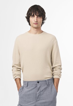 Beige langærmet skjorte i struktureret stof, rund hals, afslappet pasform. Sammen med lysegrå bukser med knap og lommer.
