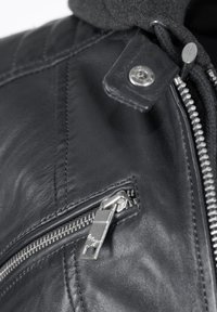 Schwarze Lederjacke mit strukturiertem Quilt-Design, mit einem silbernen Reißverschluss und Druckknopfdetails am Kragen, die strukturierte Kapuze ist sichtbar.