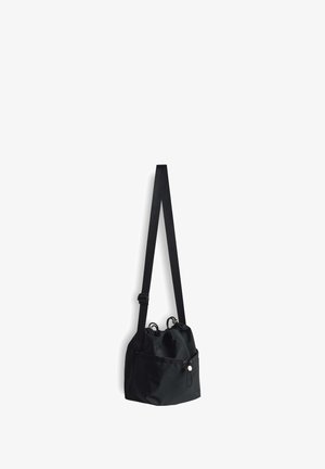 Sac bandoulière noir à cordon avec poche avant et sangle d’épaule réglable suspendu sur fond blanc.