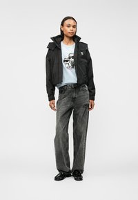 Juodas trumpas švarkas su kapišonu, šviesiai mėlynas grafiškas marškinėliai su animaciniais gyvūnais, pilkos plačios kojinės džinsai ir juodi batai. Paprastas dizainas.