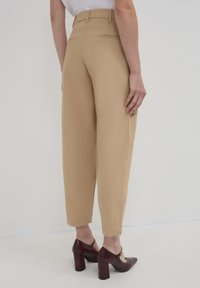 Pantaloni beige a vita alta con gamba affusolata, dotati di due tasche posteriori e cuciture pulite. Abbinati a scarpe con tacchi alti di colore rosso scuro.