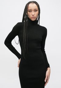 Czarna sukienka z długim rękawem i golfem, dopasowany krój, prążkowana faktura, długość do kolan, z gładkim wykończeniem tkaniny, ukazująca smukłą sylwetkę.