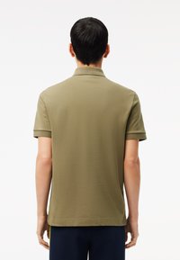 Polo shirt verde oliva con maniche corte e colletto, caratterizzato da una texture liscia e un orlo dritto, mostrato da dietro.