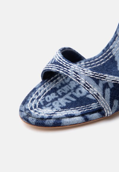 Μπλε υφασμάτινο σανδάλι με λευκές ραμμένες λουρίδες και τυπωμένο κείμενο στην εσωτερική σόλα, που εμφανίζει την περιοχή των δακτύλων και μέρος της σόλας.