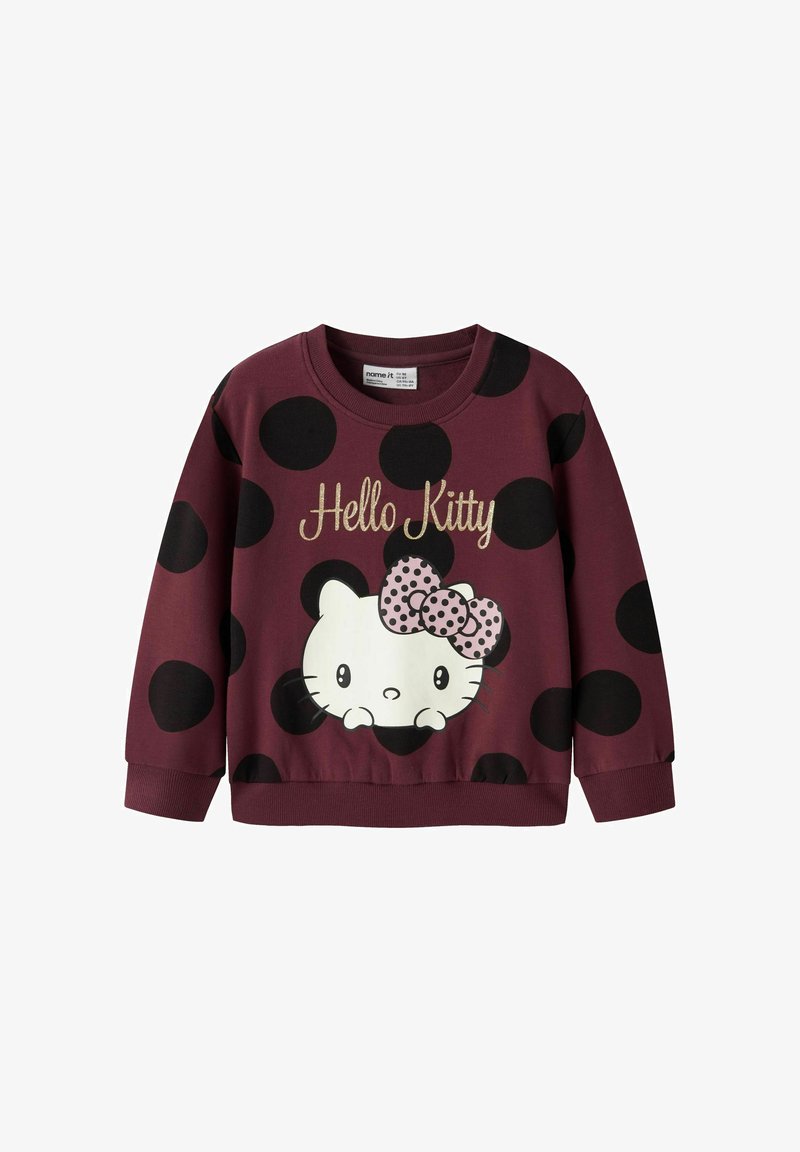 Sudadera color marrón con grandes lunares negros, que presenta un gráfico de Hello Kitty en blanco con un lazo de lunares rosas y texto dorado.