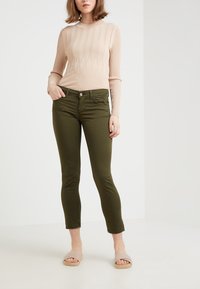 Beige geribbelde lange mouw trui, olijfgroene skinny jeans met zakken, cropped zoom en lichtgekleurde slidesandalen.