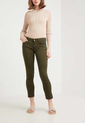 Pull en maille côtelée beige à manches longues, jean skinny vert olive avec poches, ourlet court et sandales à semelles claires.