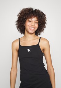 Top nero senza maniche con spalline sottili, caratterizzato da un logo bianco "cK" sul davanti. Il tessuto è liscio e aderente, esaltando la silhouette.