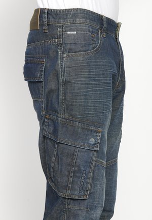 Pantalons cargo en denim bleu foncé, dotés de plusieurs grandes poches, de coutures renforcées et d'une surface texturée avec des détails de couture visibles.