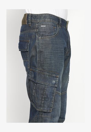 Džínsy cargo nohavice v tmavomodrej farbe, s viacerými veľkými vreckami, zosilnenými švami a štruktúrovaným povrchom s viditeľnými prešívacími detailmi.