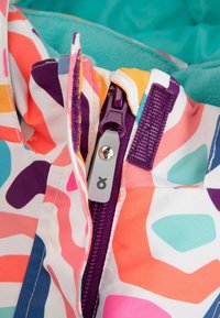 Kolorowa kurtka z abstrakcyjnymi wzorami w odcieniach różu, fioletu i niebieskiego. Posiada wyraźny fioletowy zamek błyskawiczny i miękką, turkusową podszewkę.